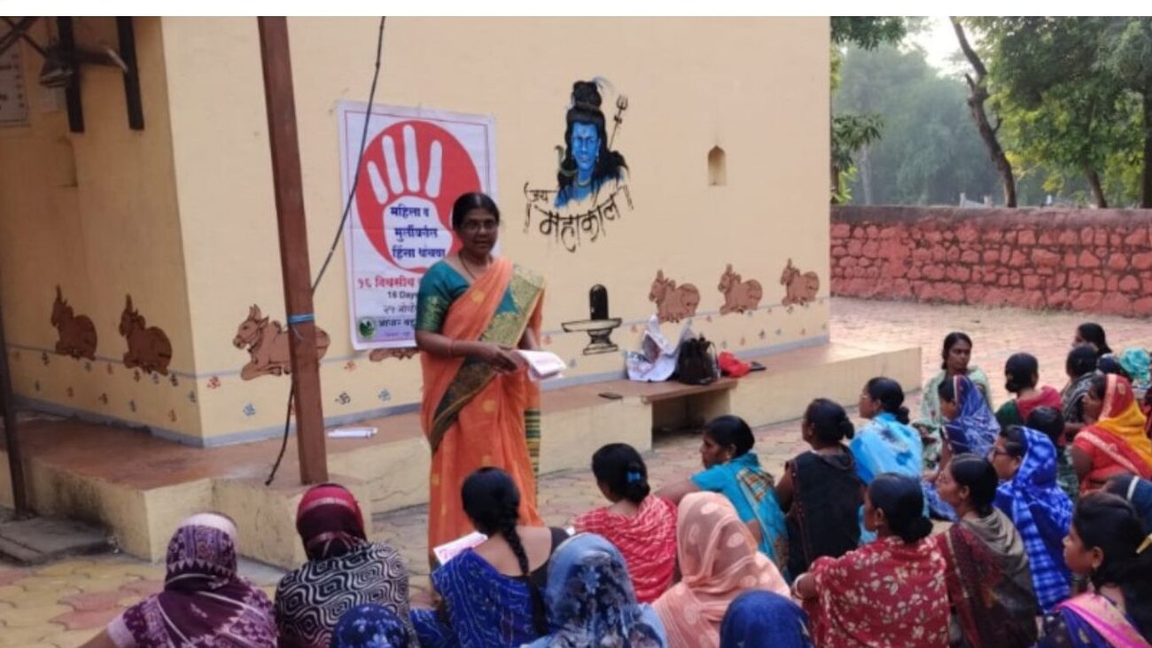 A community health worker leading a maternal health session for a large group of women seated outdoors in a village